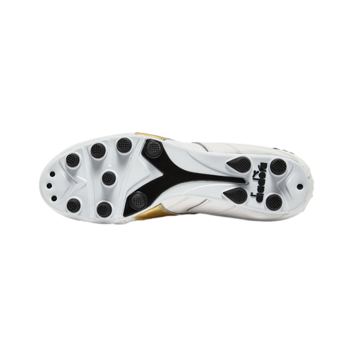Bottom view of a white Diadora soccer cleat with black studs and gold accents against a black background.