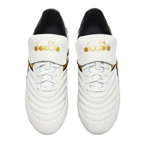 Top-down view of white Diadora soccer cleats with quilted uppers and gold branding on large fold-over tongues, against a black background.
