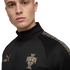 Man wearing a black Puma King track jacket with a gold Portugal national team crest and patterned shoulder detailing.