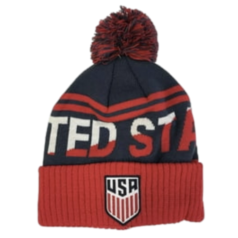 A navy and red pom-pom beanie featuring "TED STA" text and the official U.S. Soccer Federation shield logo on the red ribbed cuff.