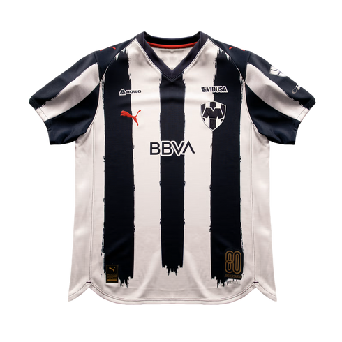 C.F. Monterrey home soccer jersey featuring navy blue and white brush-stroke stripes, red Puma logo, BBVA sponsor, and an 80th-anniversary patch.