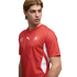 A man in a red Puma Switzerland national soccer jersey, looking to the side against a black background.