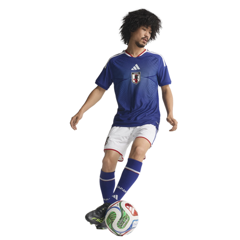 A soccer player with an afro, wearing a blue Japan national team jersey and white shorts, dribbles a soccer ball against a solid black background.