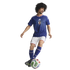 A soccer player with an afro, wearing a blue Japan national team jersey and white shorts, dribbles a soccer ball against a solid black background.