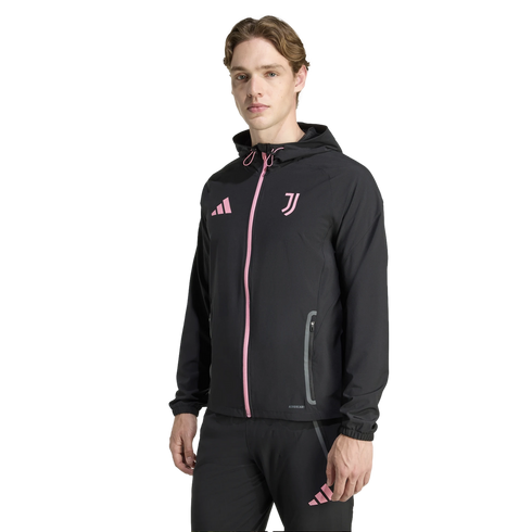 A young man wearing a black Adidas Juventus hooded track suit with pink logos and accents, standing against a solid black background.