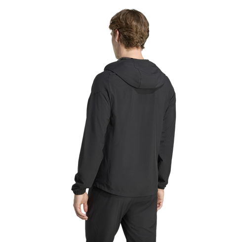 Rear view of a person wearing a black hooded athletic jacket and matching pants against a plain black background.