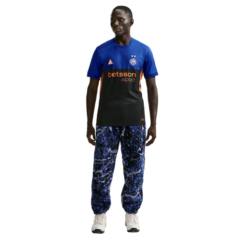 A man wearing a blue and black Inter Milan jersey, blue marble-patterned joggers, and white sneakers, standing against a solid black background.