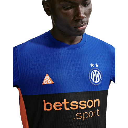 A man wearing a blue and black Inter Milan soccer jersey with orange ACG and Betsson Sport logos against a black background.