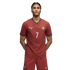 A young man with braided hair wearing a maroon soccer kit with the number 7, standing against a black background.
