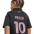 Back view of a child with braided hair wearing a black soccer jersey with "MESSI" and the number "10" printed in pink below the words "FREEDOM TO DREAM".