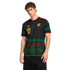 A man models a black Adidas Jamaica soccer jersey with green, red, and yellow patterns of vinyl records and sound waves.