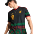 Man in a black Jamaica football jersey with vibrant green and red graphic patterns, a gold number 10, and team crest. He wears a black cap and silver necklace.