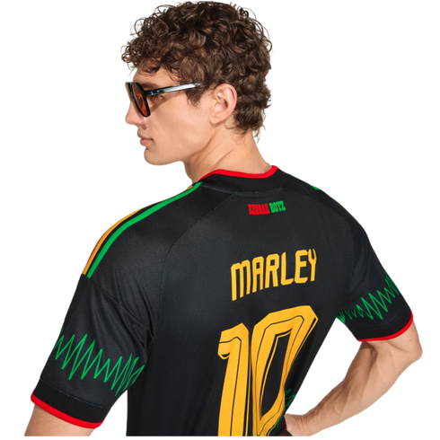A man in sunglasses seen from behind, wearing a black "MARLEY 10" Reggae Boyz jersey with green zigzag patterns on the sleeves.