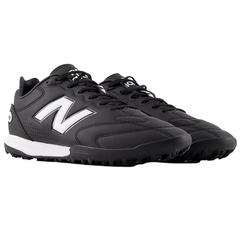 Pair of black New Balance soccer turf shoes featuring a white "N" logo and midsole, shown from a side angle against a black background.