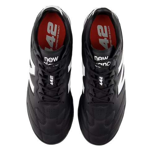 Top-down view of black New Balance 442 soccer cleats with white accents and red insoles on a black background.