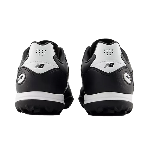 Rear view of a pair of black and white New Balance 442 turf soccer shoes against a solid black background.