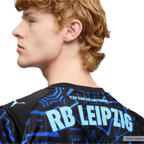 Profile of a man with wavy reddish hair wearing a black Puma jersey with "RB LEIPZIG" and "YOU CAN DO ANYTHING" printed in light blue on the back.