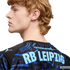 Profile of a man with wavy reddish hair wearing a black Puma jersey with "RB LEIPZIG" and "YOU CAN DO ANYTHING" printed in light blue on the back.