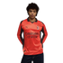 A person with curly hair wearing a long-sleeved, bright orange AC Milan soccer jersey with dark brown accents against a black background.