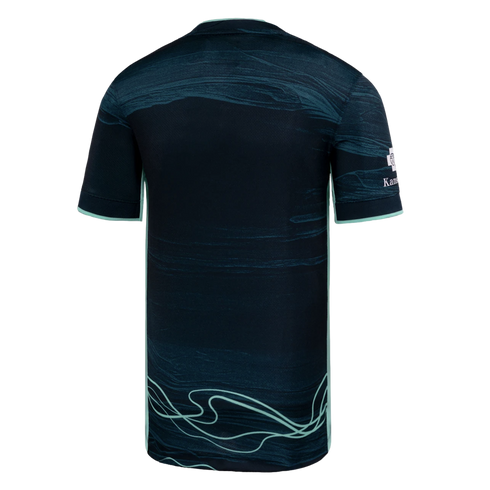 Back view of a dark teal soccer jersey featuring mint green side piping and light green wavy line graphics at the bottom hem.