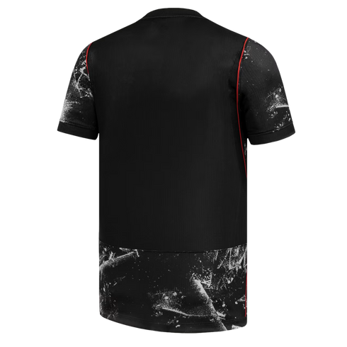 A back view of a black short-sleeved jersey with white splatter patterns on the sleeves and bottom hem, accented by thin red piping along the seams.