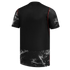 A back view of a black short-sleeved jersey with white splatter patterns on the sleeves and bottom hem, accented by thin red piping along the seams.