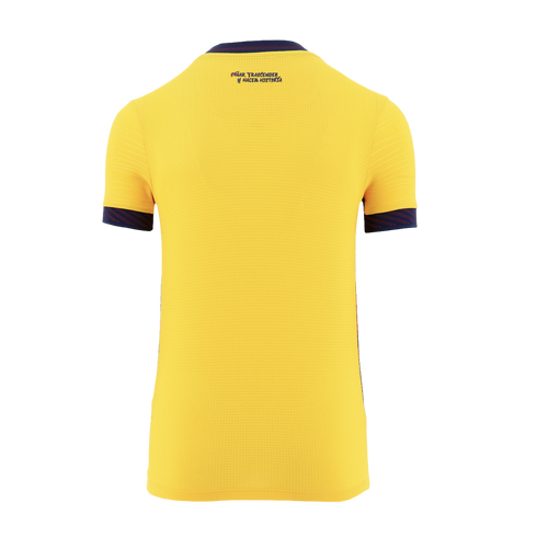 The back view of a yellow short-sleeved sports jersey against a black background. It features a navy blue collar and sleeve cuffs with a reddish-pink pattern. The Spanish phrase "SUEÑA, TRASCENDER Y HACER HISTORIA" is printed in dark blue on the upper bac