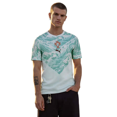 A man stands against a black background wearing a white t-shirt with a light teal abstract pattern, the Portugal national football team crest, and a small Puma logo.