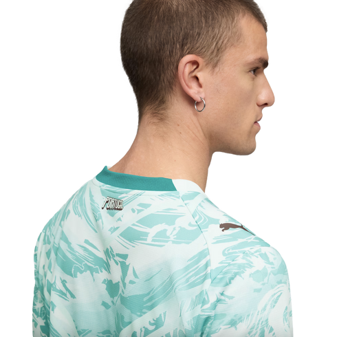 A back and side profile of a man with short hair wearing a white and teal abstract-patterned t-shirt. The shirt features a solid teal collar, the word "PORTUGAL" on the upper back, and a small Puma logo on the shoulder.
