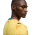 A profile view of a Black man looking over his shoulder, wearing a yellow Puma sports jersey with the flag of Ghana on the back of the neck and a patterned design on the shoulder, set against a solid black background.