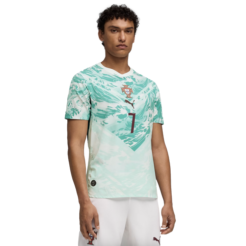 A young man models a white and light green abstract-patterned soccer jersey with a central crest and the number 7, paired with white shorts, against a black background.