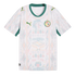 A white Senegal national football team away jersey featuring a green V-neck collar and sleeve trim. The shirt has a faint, multi-colored geometric and lion-head pattern across the front, with the Puma logo on the right chest and the Senegalese football fe