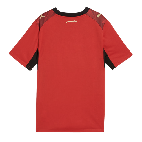 A back view of a red short-sleeved Puma jersey with black trim around the collar and underarms. It features gold Puma logos on the shoulders and gold Arabic calligraphy on the upper back against a black background.