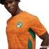A close-up of a man wearing an orange Côte d'Ivoire national football team jersey against a black background. The jersey features a tonal animal-print pattern, green mesh panels on the sides, and the team's crest on the chest, which includes a white eleph