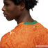 A profile view of a young man with dark curly hair wearing an orange Puma jersey against a black background. The jersey features a tonal abstract animal print, a white Puma logo on the shoulder, and a green collar with a small flag of the Ivory Coast on t