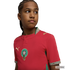 A young person with braided hair looking to the side, wearing a red Morocco national football team jersey by Puma, against a solid black background.