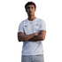 A waist-up portrait of a young man with curly hair posing with his arms crossed against a solid black background. He is wearing a white Puma jersey with a subtle, light-grey tonal swirl pattern. The jersey features a black Puma logo on the right chest and