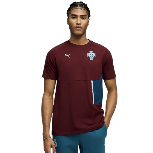 A young man with braided hair models a maroon Puma short-sleeve shirt featuring the Portugal national team crest and a teal side pocket detail, set against a solid black background.