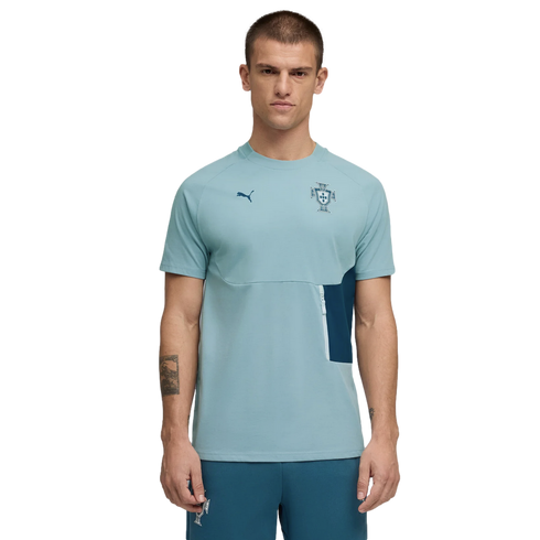 A studio photograph of a man modeling a light teal short-sleeved Puma training t-shirt with a Portuguese Football Federation crest on the chest, paired with matching teal pants, against a solid black background.