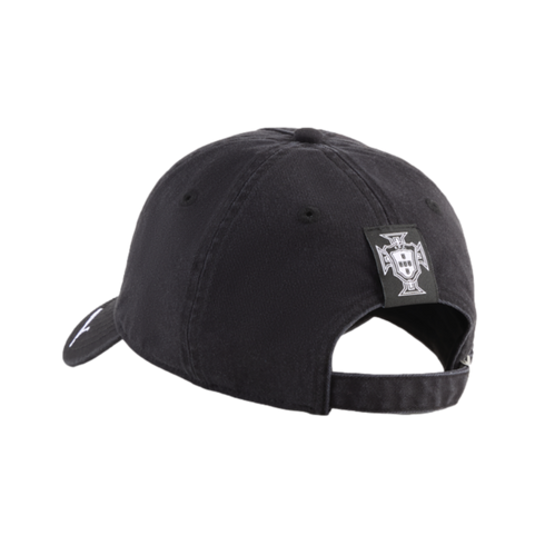 A rear-side view of a black baseball cap featuring a small white crest logo on a square patch above the adjustable strap, set against a solid black background.