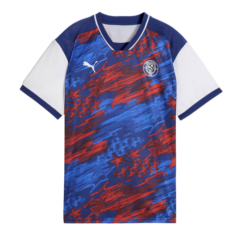 A short-sleeved Puma soccer jersey featuring a blue and red abstract pattern with stars. It has white sleeves with blue cuffs and a blue V-neck collar with white piping.