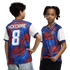 A boy and a girl model a red, blue, and white abstract-patterned soccer jersey against a black background. The boy on the left shows the back of the shirt, which features the name "MCKENNIE" and the number "8" in white. The girl on the right shows the fro
