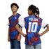 A studio portrait against a black background shows two young children modeling a blue and red Puma soccer jersey. The boy on the left faces forward, showing the front of the jersey with its abstract star pattern and Puma logo. The girl on the right faces