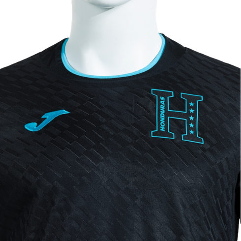 A close-up of a black Honduras national soccer team jersey by Joma, featuring a light blue crew neck, a subtle textured pattern, and the team crest and brand logo on the chest.