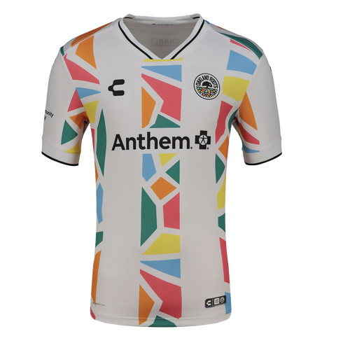A white Oakland Roots soccer jersey featuring a colorful geometric mosaic pattern in orange, blue, pink, yellow, and green running vertically down the center and along the sides. The jersey includes the "Anthem" sponsor logo across the chest, the team cre