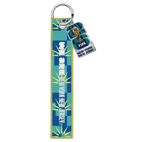 A FIFA World Cup 2026 keychain featuring a long, embroidered blue and teal fabric strip with vertical white text reading "WE ARE NEW YORK NEW JERSEY." A smaller dangling tag shows the official tournament logo, the World Cup trophy, and the host city names