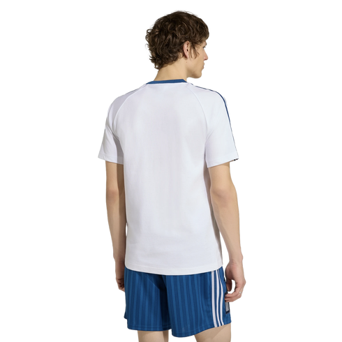 Rear view of a man in a white t-shirt with blue trim and blue striped athletic shorts against a black background.