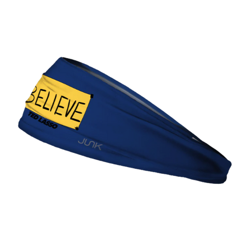 A navy blue Junk headband featuring a yellow "BELIEVE" sign and "TED LASSO" text, shown at an angle against a black background.