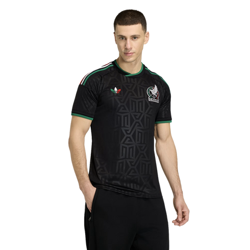 A man models a black Adidas Mexico national team soccer jersey with green trim and geometric patterns, standing against a plain white background.