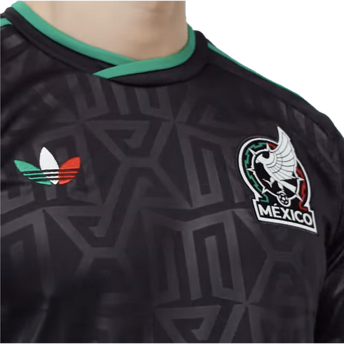 Close-up of a black Mexico national football team jersey with a subtle geometric pattern, featuring the team crest and a green, white, and red Adidas trefoil logo.